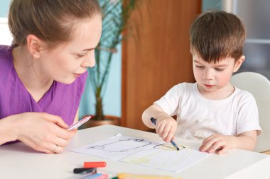 Konsantre küçük erkek çocuk kırpılmış shot renkli marker tutar ve kendisi tarafından güzel resim yapar, ona yardımcı olur ve ilginç bir şey, rahat iç iç söyler annesinin oturur