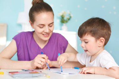 Yetenekli çalışkan küçük çocuk fotoğrafı ile büyük arzusu resim çizer, renkli marker, neşeli anne yardımcı olur renkleri seçmek, mavi duvar odadaki karşı birlikte oturmak için kullanır. Yaratıcılık ve sanat