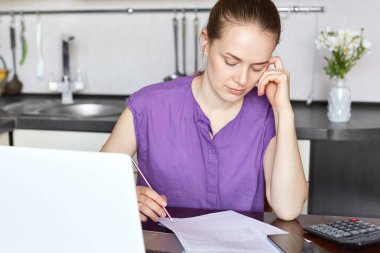 Hoş kayıtsızca, belgelerde, konsantre giyinmiş hiç makyaj ile kadın arıyorum kırpılmış atış aile bütçesine hesaplar, inşaat üstünde taşınabilir dizüstü bilgisayar, rahat mutfakta oturuyor.