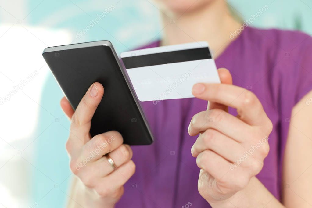 Selective focus on woman`s hands hold modern black cell phone and plastic card, makes shopping online or checks her bank account in internet, connected to wifi. People and online transactions