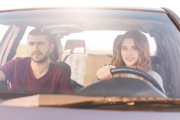 Couple travelers reach destination at car: beautiful smiling woman at wheel teaches to drive, her husband sits at front seat, controls everything. Girlfriend, boyfriend spend time together, have trip