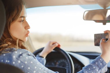 İyi görünümlü kadın pozlar yatay atış lüks araba, direksiyonda selfie akıllı telefon, oturur için kamera Face yapar ve sosyal ağlar fotoğrafları paylaşır, ücretsiz internet bağlantısı kullanır