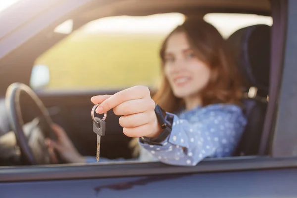 有吸引力的年轻女性持有汽车钥匙 是新汽车的快乐车主 背景模糊 可爱的妇女卖车 做广告 显示钥匙在照相机 坐在轮子 有旅途在路 — 图库照片