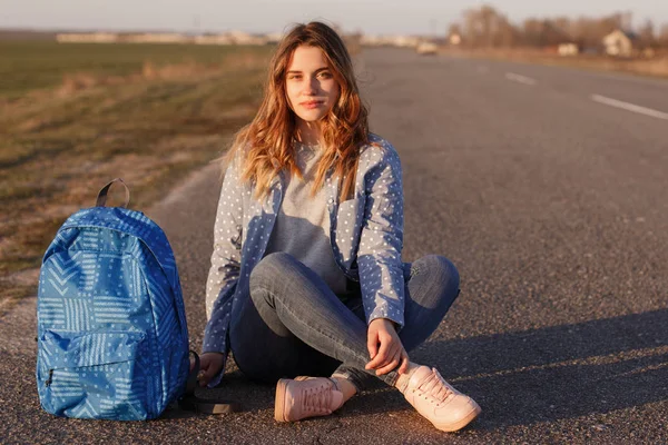 Σοβαρό Γυναικείο Hitchhiker Κάθεται Σταυρωμένα Πόδια Ασφαλτοστρωμένο Δρόμο Την Τσάντα — Φωτογραφία Αρχείου