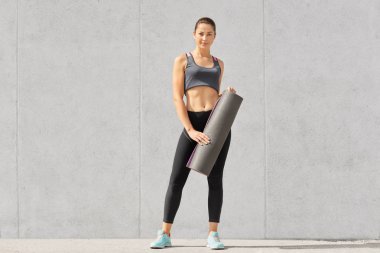 Fotoğraf kendini rahat top, tozluk ve sportshoes, giymiş kadın vücut geliştirmeci mat elinde, egzersizleri, beton duvardan izole olacak tutar belirlenir. İnsanlar, spor, motivasyon kavramı