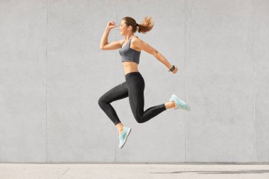 Güzel sportwoman ile at kuyruğu, sağlıklı cilt, atlar, havada rahat en iyi giyinmiş ve tozluk, gri arka plan üzerinde pozlar smartwatch giyer. İnce athleteic kız jimnastik vardır. Sağlıklı yaşam tarzı