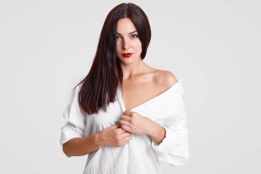 Mükemmel temiz cilt, güzel genç bir bayanla kırmızı ruj vardır, gevşek beyaz gömlek giyer, çıplak omuz gösterir, kocası ile flört ediyor, doğrudan kamera stüdyo arka plan üzerinde izole, ciddi bakar