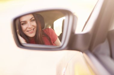 Çekici genç kadın modeli ile nazik bir gülümseme, Araba, kırmızı elbiseler giymiş yan dikiz aynasında bakar, otomobil sürücüleri, arkadaşlarınızla uzun yolculuk vardır, yüksek hızlı sahiptir. Yaşam tarzı kavramı