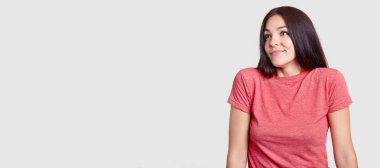 Stüdyo atış olan koyu saçlı, çekici rüya gibi kadın görünüyor bir yana, rahat t gömlek, pozlar sol promosyon içeriği veya reklam için boş alan ile beyaz arka plan karşı giymiş