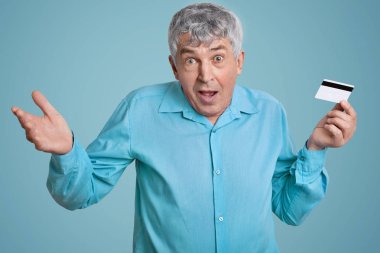 Kırışıklıklar yüzünde, gri saçlı, şaşkın olgun buruşuk adamla şaşkınlık içinde omuz silkiyor, ne satın almak bilmiyor, plastik kart tutan, online alışveriş yapar. İnsanlar ve surprisement kavramı