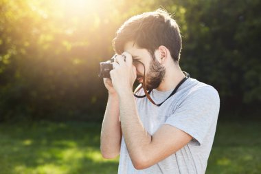Yaz yaşam tarzı görüntü fotoğrafları ile retro kamera ayakta yana doğru birisi fotoğraf çekimi yapma sakallı adam. Genç fotoğrafçı rahatlatıcı yeşil park veya Grönland resim yapma kamera ile