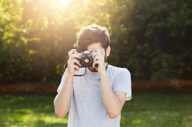 Genç erkek fotoğraf fotoğrafları ile duran yeşil çimen, vintage fotoğraf makinesi yapma. Profesyonel erkek biri ondan önce fotoğraf çekme retro kamerayı kullanarak. İnsanlar, hobi ve dinlenme kavramı