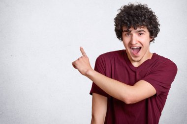 Pozitif kıvırcık adam ağız açık tutar, mutluluktan exclaims, kenara boş kopya alanı reklam içeriği için puan, rahat t gömlek, Hey, göz sol tarafta, lütfen giyer. Reklam kavramı