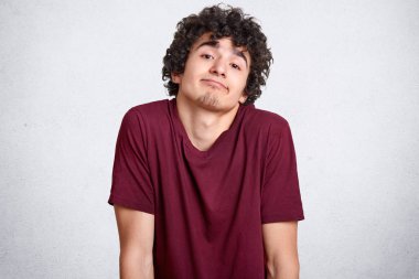 Şaşkınlık, çantalar dudaklar, tereddüt clueless genç shruggs omuz seçmek ne bilmiyor, şüpheli geliyor, beyaz beton duvara teşkil etmektedir. İnsanlar, gençlik, belirsizlik kavramı.