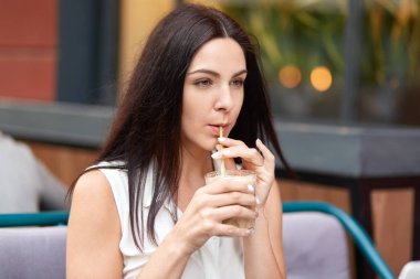 Düşünceli çekici kadın yatay açık atış gün kapalı, açık Cafe pozlar sahiptir, muzlu süt içiyor, beyaz bluz giymiş, kameraya odaklı, boş zaman vardır. İnsanlar ve eğlence