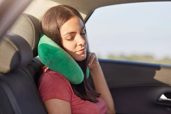 Female passenger sleeps in car while rides on long distance, uses small pillow as has pain in neck, takes nap, has rest, feels tired for being in motion much time. People and travelling concept