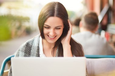 Neşeli memnun beyaz bir kadın fotoğrafı olumlu görünüyor dizüstü bilgisayar ekranında, yorgan vardır, komik hikayeler Web sitesinde okur, açık kafede teşkil etmektedir. Kavram insanlar, eğlence, dinlenme.