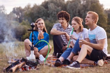 Mutlu şirket gülümseyen var piknik birlikte, duman nargile, şenlik ateşi oturur, birbirleri ile iletişim, alkolsüz içecek, ifadeler tatmin olması. Arkadaşları ve boş zaman zaman kavramı