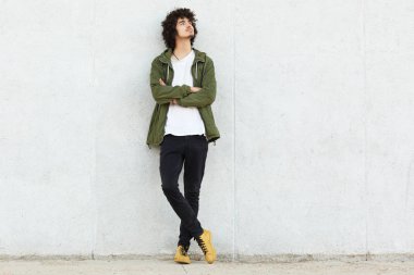 Düşünceli rüya gibi cool adam çekim yeşil şık anorak, spor ayakkabı giyer, katlanmış silah tutar, dalgın bakmak ile baş yükseltir, beyaz arka plan kopya alanı metni ile poz veriyor.