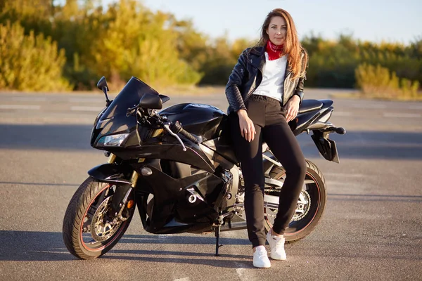 魅力的な女性の写真が本当の冒険屋外 バイカーの服を着たバイクの近くに立って 晴れた日と穏やかな雰囲気を楽しんでいます オートバイのコンセプト 乗車のための時間 — ストック写真