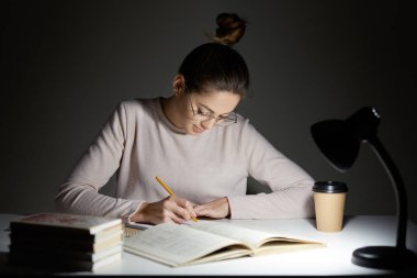 Busy freelancer rewrites infrormation into notepad, prepares article for publication, reads books, writes some notes in organizer, drinks takeaway coffee, sits in darkness, wears round big spectacles clipart