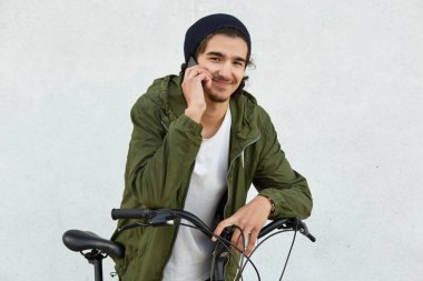 Küçük sakallı neşeli genç kız akıllı telefon üzerinden hoş konuşma vardır, anorak ve şık şapka giyer, onun bisiklet eğilir, yüz ifadesi, aktif yaşam tarzı memnun