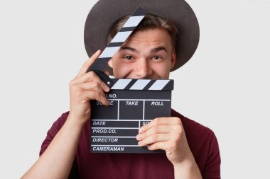 Pozitif genç kameraman fıçı tahtası yakınındaki yüz tutan, neşeli ifadesi olan, şapka giyer, kesit, filme, pozlar beyaz stüdyo duvar karşı yer yapmak için hazırlar. Sinematografi kavramı