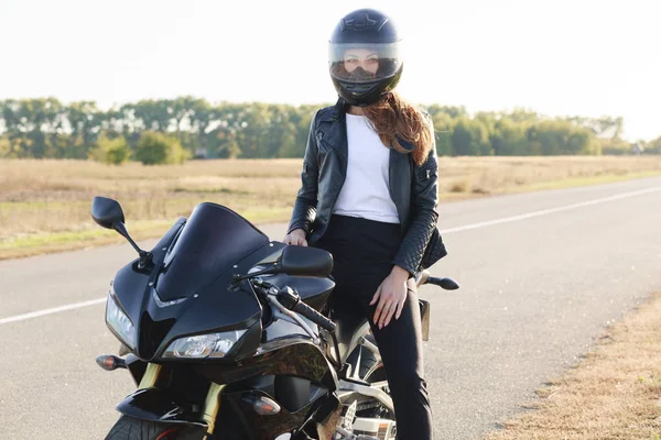 ストリート スタイルのコンセプトです アクティブなプロライダー ヘルメット 黒い革のジャケットを身に着けている 道路で Motorrbike のポーズ 高速で長い距離をカバーして 旅行準備を楽しんでいます — ストック写真