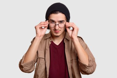 Emin yakışıklı sakallı kıvırcık adam ellerini gözlük kenarında tutar, dikkatle, siyah şapka ve bej gömlek, beyaz arka plan karşı modelleri giyinmiş görünüyor. İnsanlar ve yüz ifadeleri kavramı