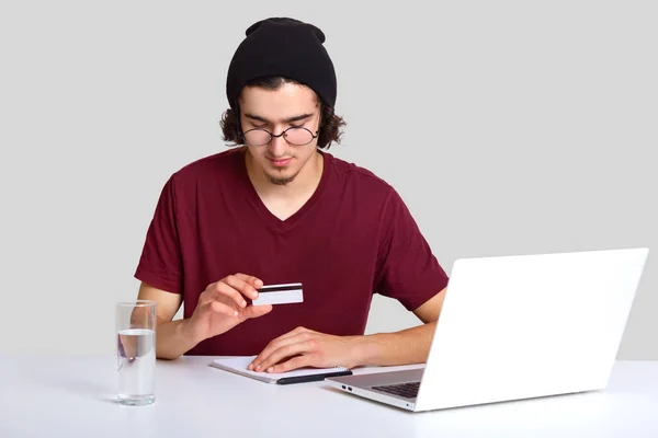 気配りのあるハンサムな男性が巻き毛を支払うかクレジット カード ラップトップ コンピューター上で動作 新鮮な水のガラスとの取引は 白い背景で隔離するつもり 購入の概念 — ストック写真
