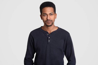 Ciddi Afro adam rahat kazak giymiş, kendi kendine güvenen ifadesi olan, doğrudan kamera, beyaz arka plan üzerinde izole bakar Amerikan. Stüdyoda etnik erkek teşkil etmektedir. Yüz ifadeleri kavramı