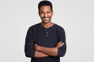 Katlanmış, kollu yakışıklı memnun siyah adam kapalı atış rahat kıyafetler giyer, hafifçe gülümsüyor, Afro saç kesimi vardır, muhatap ile hoş konuşma vardır üzerinde beyaz duvar izole. Olumlu duygular