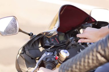 Tanınmayan aktif kadın motosikletçi kırpılmış atış motoru başlatmaya çalışırsa, anahtar üzerinde döner, şehirlerarası yolda kapsar, deri ceket giyer. Kişi, sokak stili, hobi ve aşırı kavramı