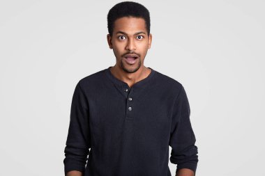 Kızgın şaşkın koyu tenli Genç adam surprisement rahat jumper giyinmiş, ağız açılır, beyaz arka plan üzerinde izole muhatap, ani haber tepki verir. Erkeklik kavramı