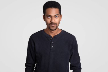 Kapalı atış ciddi öz kıvırcık kısa saçlı Genç adam koyu tenli emin sert ifadesiyle modelleri beyaz arka planı kapalı görünüyor. İnsanlar, etnik yapı ve yaşam tarzı kavramı