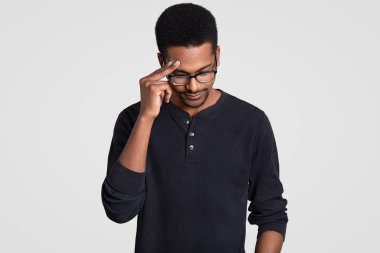 Stresli yorgun overworked erkek işçi koyu tenli, el başına tutar, tepeden bakıyor, şeffaf gözlük ve rahat jumper giyer, beyaz arka plan üzerinde izole düşüncelerle toplamak çalışır