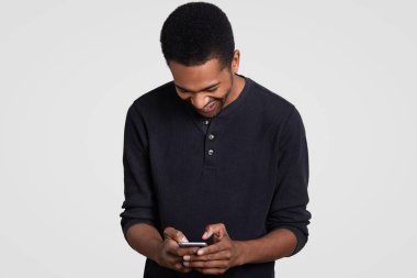 Afro saç kesimi, koyu tenli adamla çok memnun mutlu güler, cep telefonu, hücresel, türleri görüşlere okuma komik hikaye rahat kıyafetler, modelleri beyaz arka plan üzerinde giyer almıştır. Mutluluk kavramı