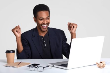 Zengin işadamı başarısını kutluyor, yumruk zafer jest, başlangıç proje bitirmek memnun olarak yükseltir, resmi elbise giyer, masaüstü gözlük, paket servisi olan restoran kahve, Not defteri, dizüstü oturur