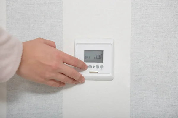 Smart home concept. Hands puches button switch on white wall, regulates temperature in flat or room. Close up, selective focus. Control panel