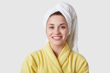 Gülümseyen beyaz bir genç kadın en az makyaj, beyaz pefect dişler, sağlıklı yumuşak cilt vardır, rahat sarı bornoz giymiş beyaz arka plan üzerinde güzellik bakımları salonda, modelleri için hazırlar