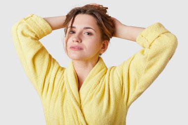 Neşeli ifade ile rahat güzel genç bayan, yavaşça, gülümsüyor toplar elle, güvenle kamera sarı bornoz içinde giyinmiş, bakar ıslak saç taze, temiz banyo duş alma sonra hissediyor
