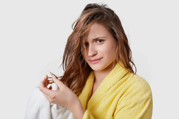 Women and problems with hair concept. Unhappy young Caucasian beautiful woman has wet hair, discontent with lotion or new shampoo, wears bathrobe, stands against white background, takes shower