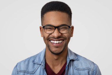 Karanlık görüntüsünü yakından geniş dişlek gülümseme, beyaz dişler adamla derili, kot gömlek, gözlük takıyor, kısa kıvırcık saçlı, komik fıkra güler, mutluluk ifade eder, stüdyoda yalnız modelleri