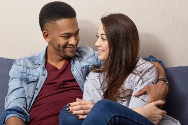 Fotoğrafı çok ırklı genç aile kucaklama ve gülümseme olumlu, beraberlik zevk, rahat kanepe poz, yeni daire satın sevinirler veya düz hoş bir şey tartışmak mutlu anne hazır hale