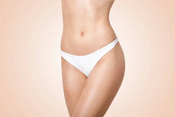 Horizontal shot of slim young woman with perfect body shape, wears white panties, has fit figure, shows nude stomach, keeps to healthy diet, demonstrates results of weight loss. Slimming concept