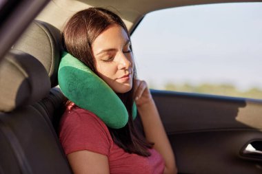 Yorgunluk esmer kadın kullandığı araba, seyahat yorgun için bak, rahat t gömlek, pozlar otomobil, yeşil yastık giymiş uykuda düşüyor. Kişi, turizm ve seyahat kavramı. Erkek konfor sahiptir