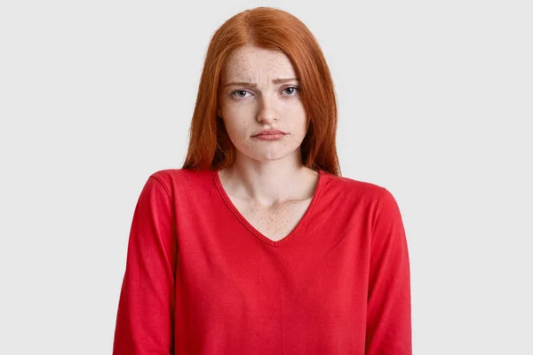不機嫌な生姜女性顔をしかめ 肌にそばかすのある Doenst の負の感情を表現する何か 白い背景の上のモデルのような赤いジャンパーを着ています 人間の表情や感情 — ストック写真