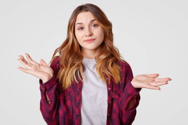 Clueless ifade ile tereddüt genç kadın, shruggs omuz karışacak, giyer kareli gömlek, yüzleri zor soru, dalgalı saç, stüdyo beyaz arka plan üzerinde izole vardır. Ne seçmek için?