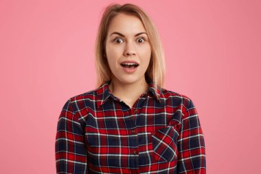 İzole shot sürpriz hafif saçlı Genç kadın tutar ağız yaygın olarak açılan, kareli gömlek giymiş, pembe bir arka plan karşı teşkil etmektedir, korku ve şaşkınlık ifade eder. Yüz ifadeleri kavramı
