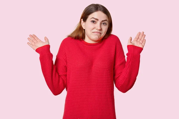 愤怒的欧洲年轻女子举起手掌 感觉不被证明 穿着随意的红色毛衣 姿势在玫瑰色的背景 有无线索的表情 站在室内 人与不确定性概念 — 图库照片